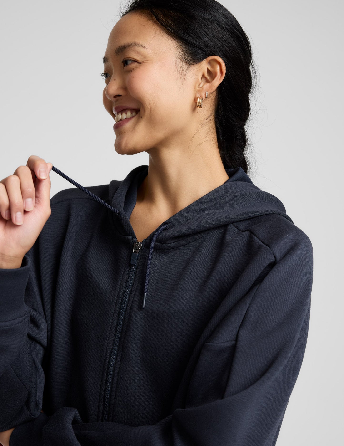 Woman is wearing a blue zip-up jacket and shorts against a plain background.