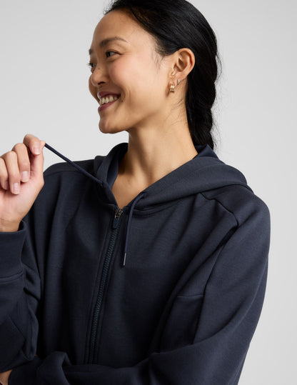 Woman is wearing a blue zip-up jacket and shorts against a plain background.