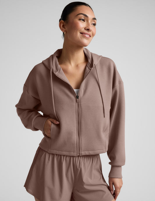 Woman wearing a brown full zip jacket and shorts against a plain background.