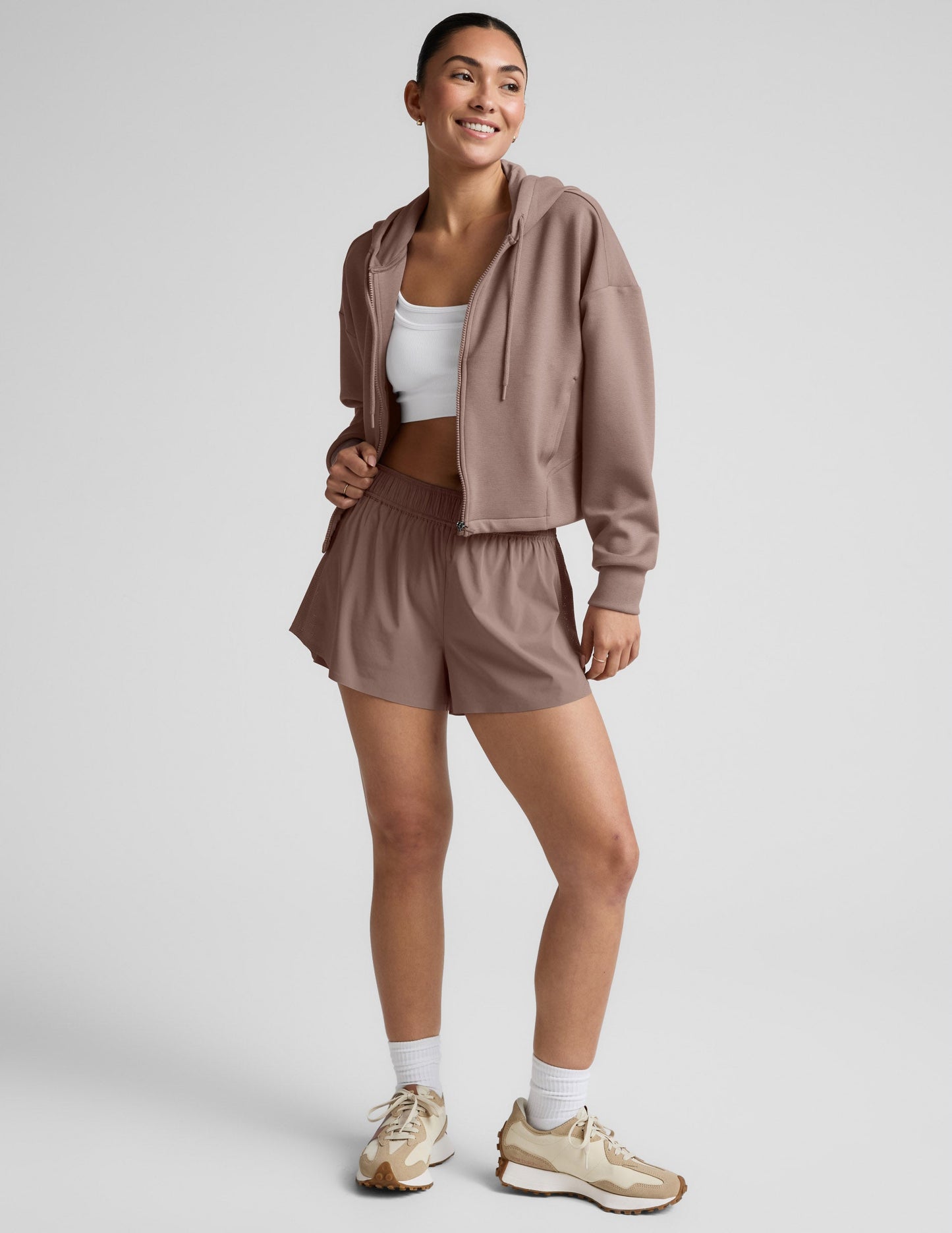 Woman wearing a brown full zip jacket and shorts against a plain background.
