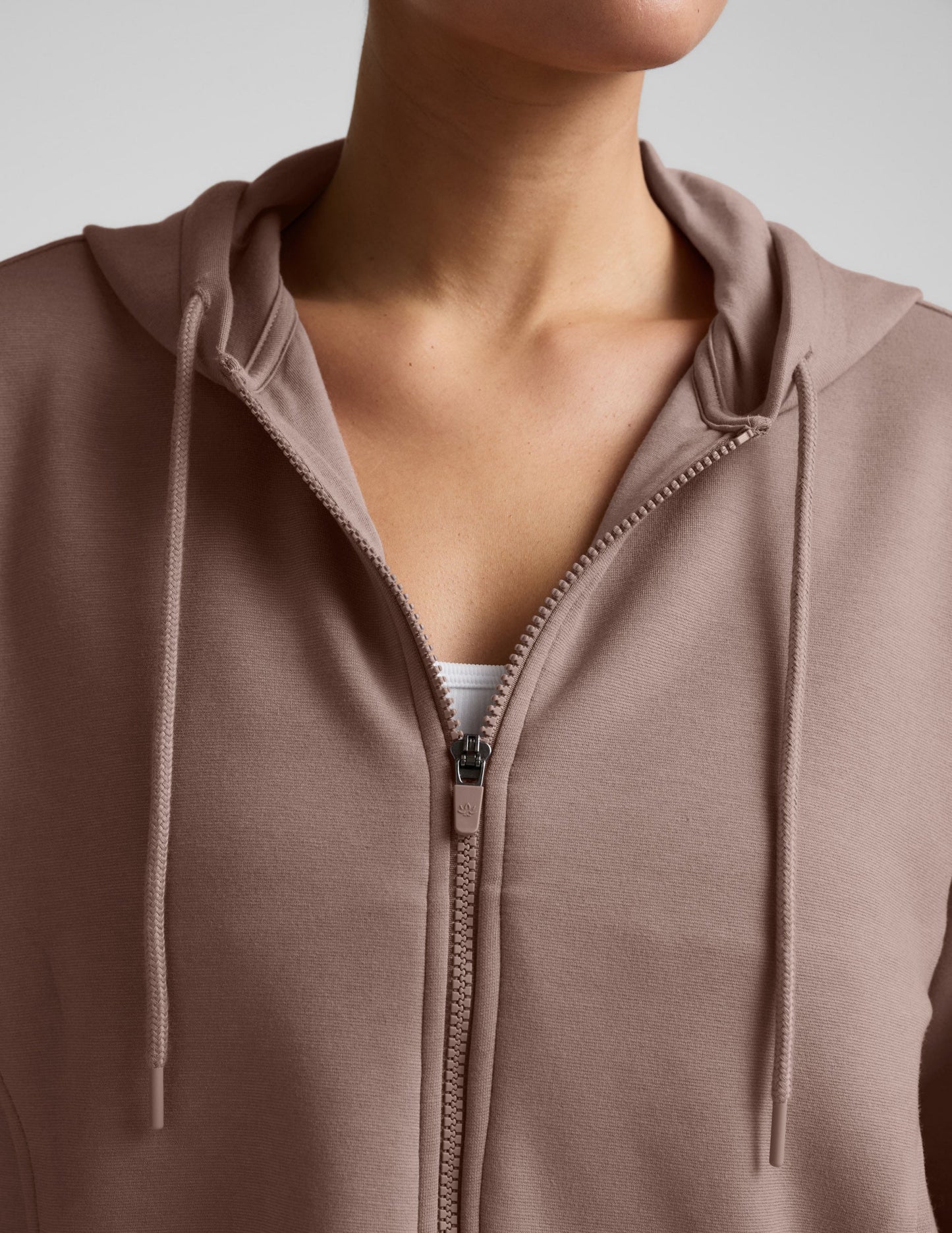 Woman wearing a brown full zip jacket and shorts against a plain background.