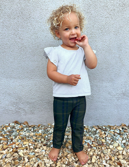 Toddler wearing Dark Olive Preppy Plaid SoftMark Toddler Legging with a green check pattern, standing barefoot on gravel.