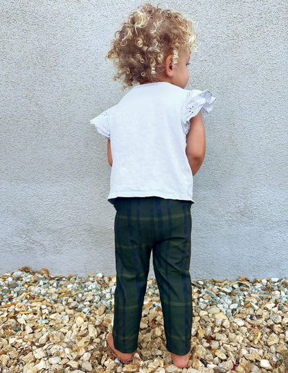 Back view of a toddler wearing Dark Olive Preppy Plaid SoftMark Toddler Leggings, standing on gravel against a gray wall.