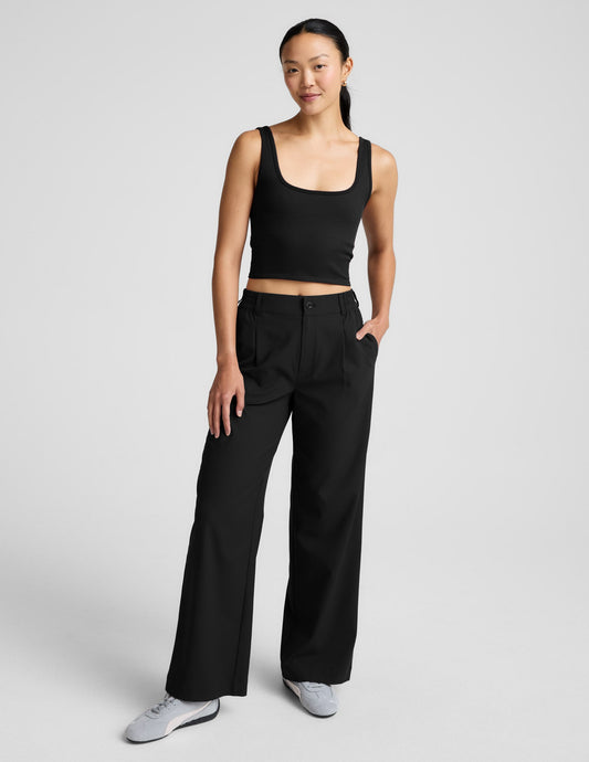 Woman is wearing a black ribbed tank and pants against a light gray background.