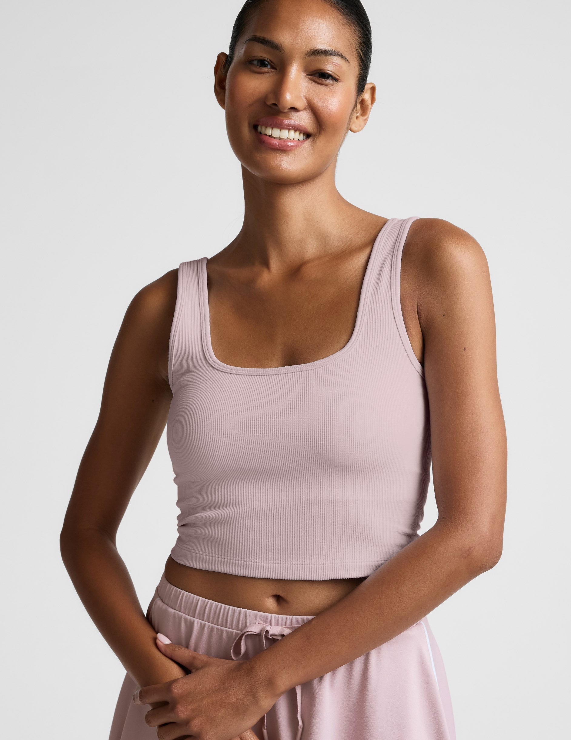 Woman wearing a pink ribbed cropped tank and skirt against a plain background.