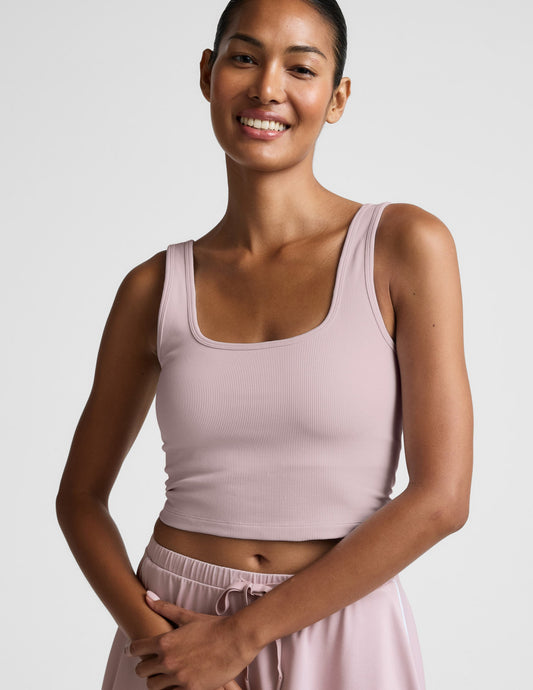 Woman wearing a pink ribbed cropped tank and skirt against a plain background.