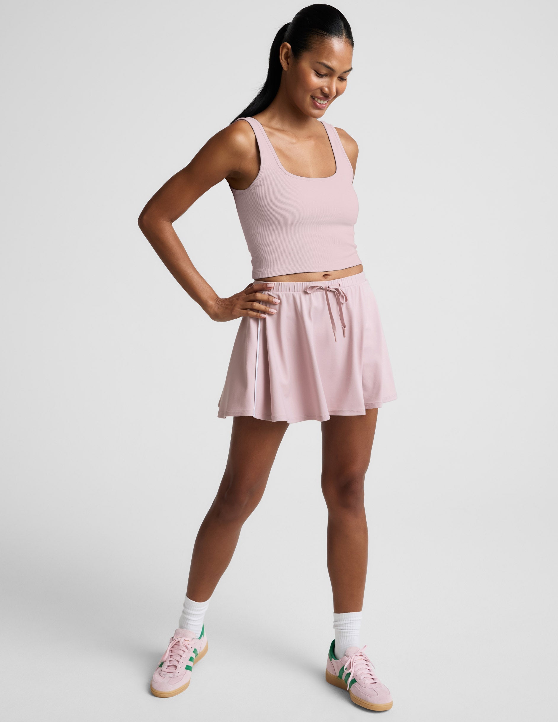 Woman wearing a pink ribbed cropped tank and skirt against a plain background.