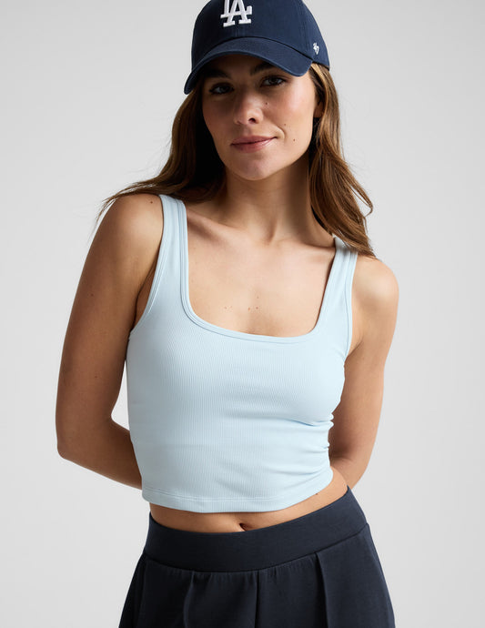Woman wearing a blue cropped tank and blue pants against a plain background.