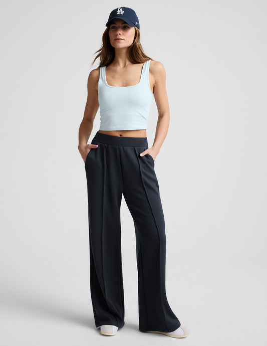 Woman wearing a blue cropped tank and blue pants against a plain background.