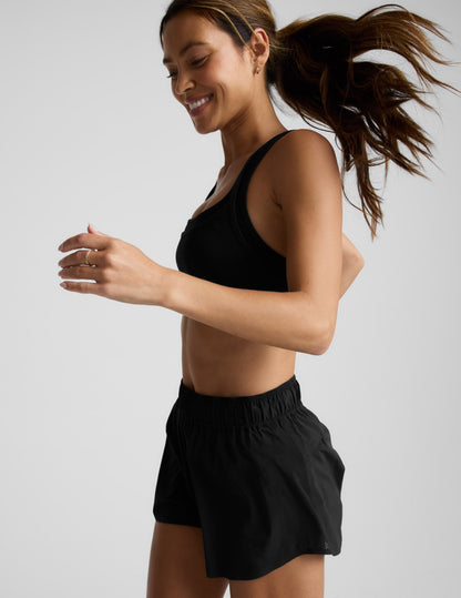 Woman running in black Solemate 2.5" Short with side mesh panels and elastic waistband in a side-profile view.