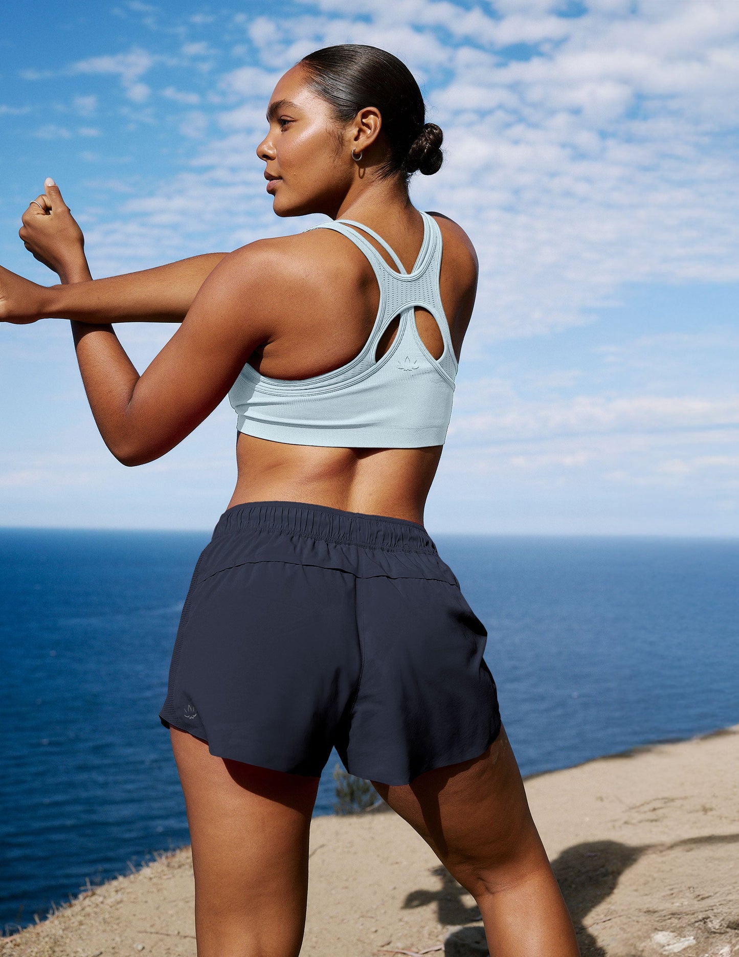 Rear view of Navy Solemate 2.5" Short on a woman stretching by the ocean; features an elastic waist and relaxed fit.