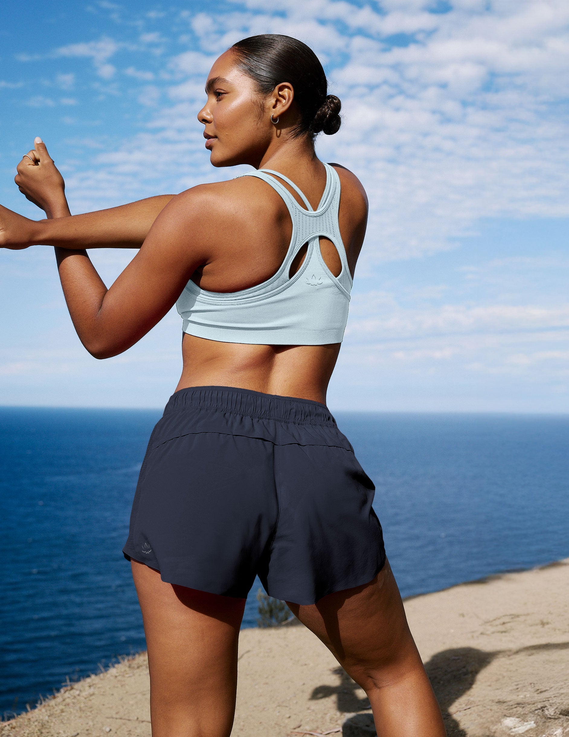 Rear view of Navy Solemate 2.5" Short on a woman stretching by the ocean; features an elastic waist and relaxed fit.