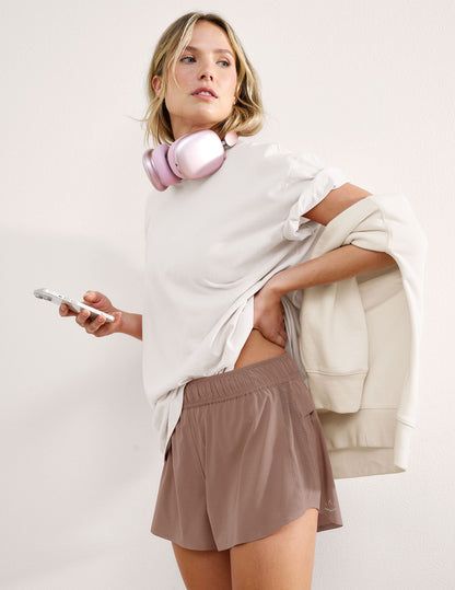 Brown Solemate 2.5" Short with perforated side panels and elastic waist on a model with white tee and pink headphones.