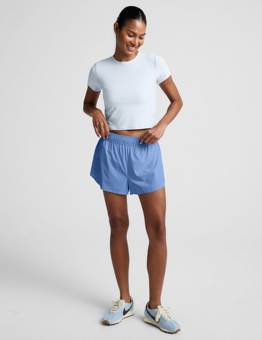 Blue Solemate 2.5" Short on a smiling woman. Mid-rise dolphin running shorts with a gathered elastic waistband and liner.