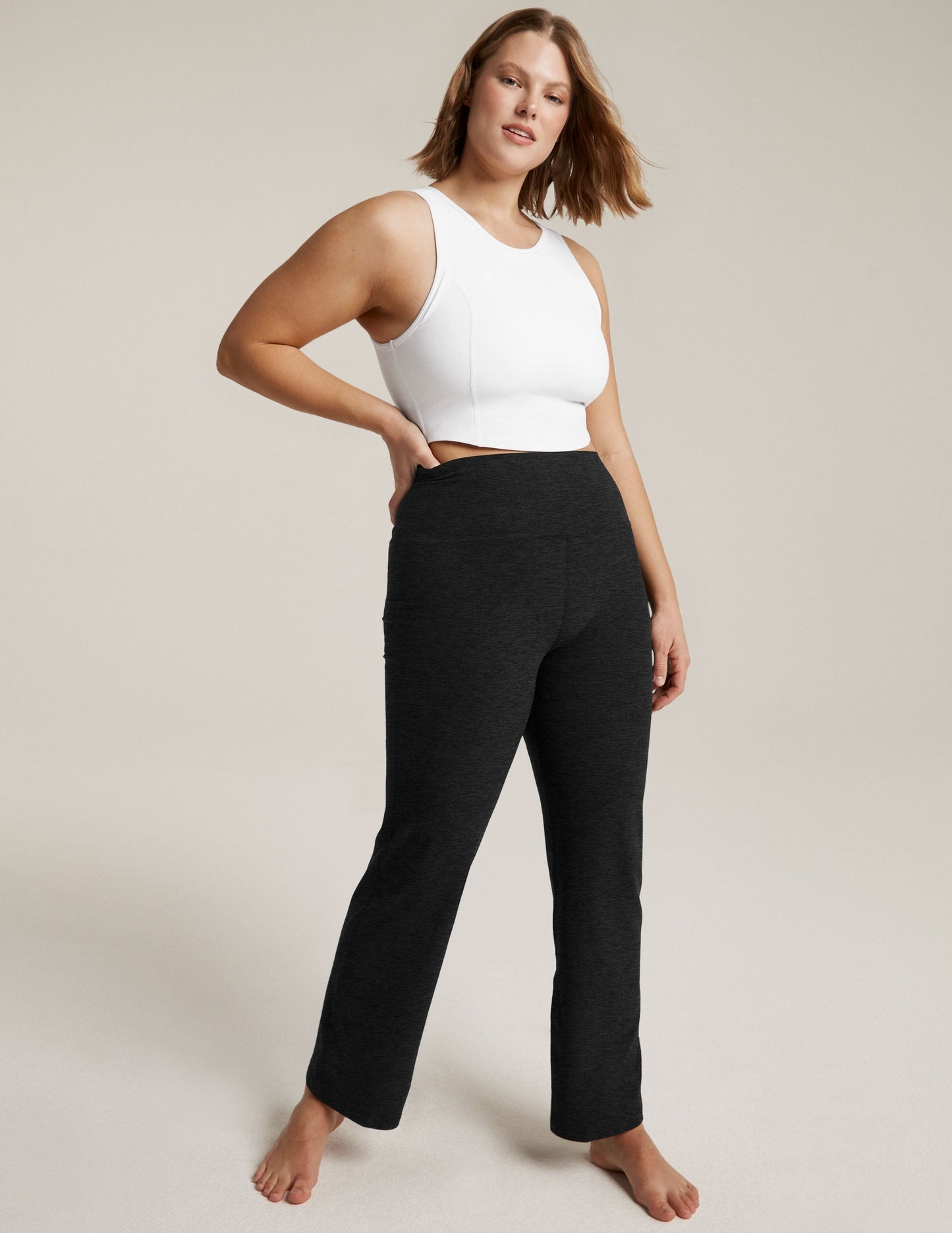 Woman models black marled Spacedye Practice High Waisted Pant with a white crop top, high-rise fit and bootcut leg.