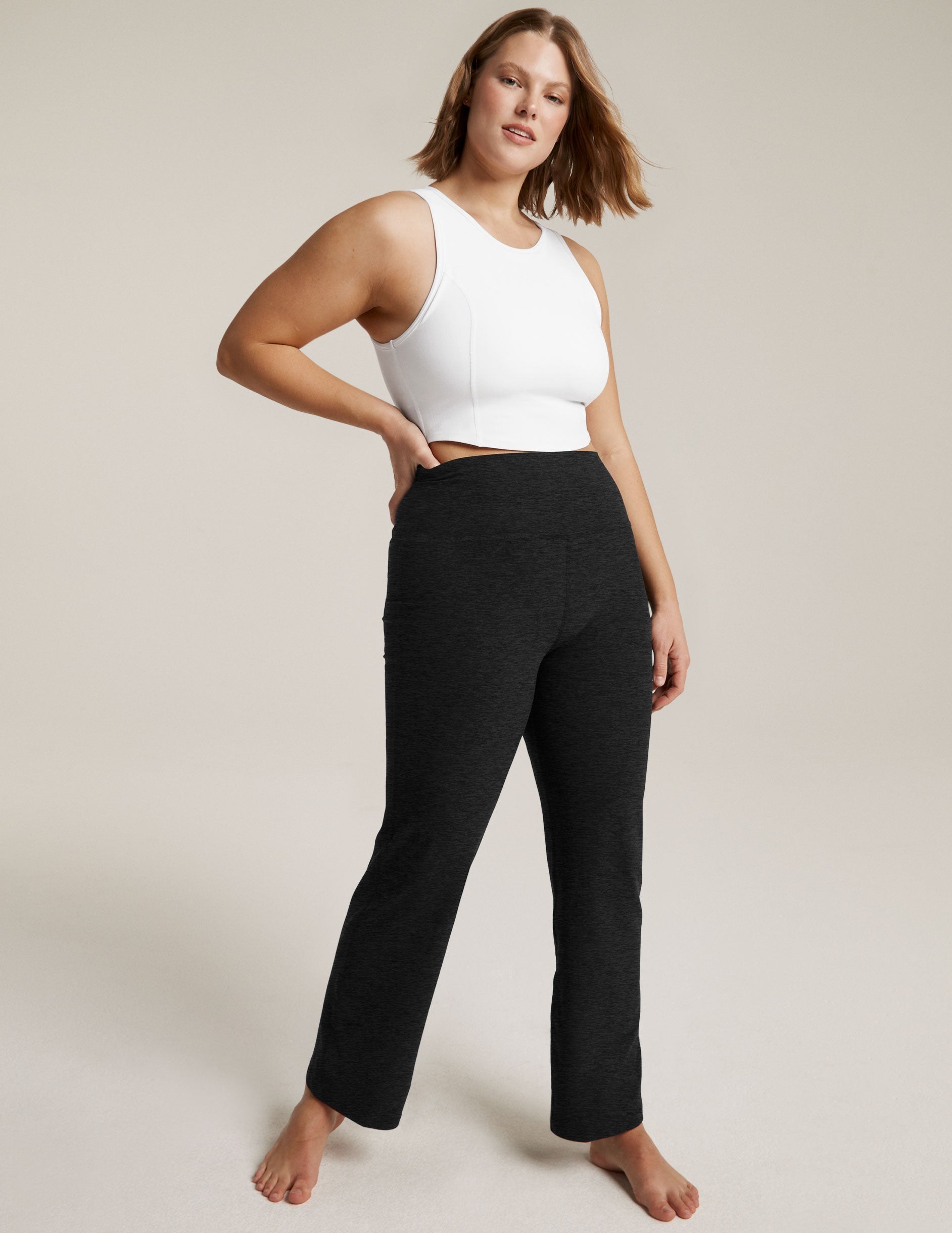 Woman models black marled Spacedye Practice High Waisted Pant with a white crop top, high-rise fit and bootcut leg.