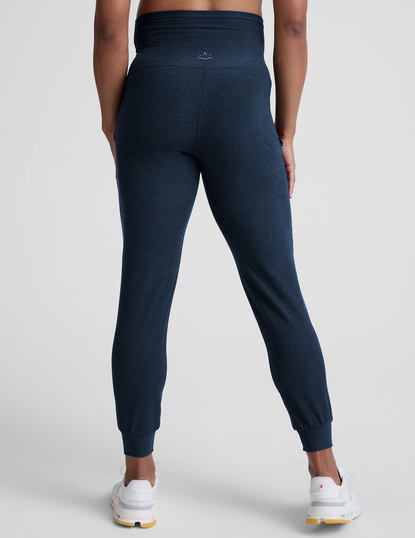 pregnant woman wearing navy blue maternity joggers with pockets on a plain background.