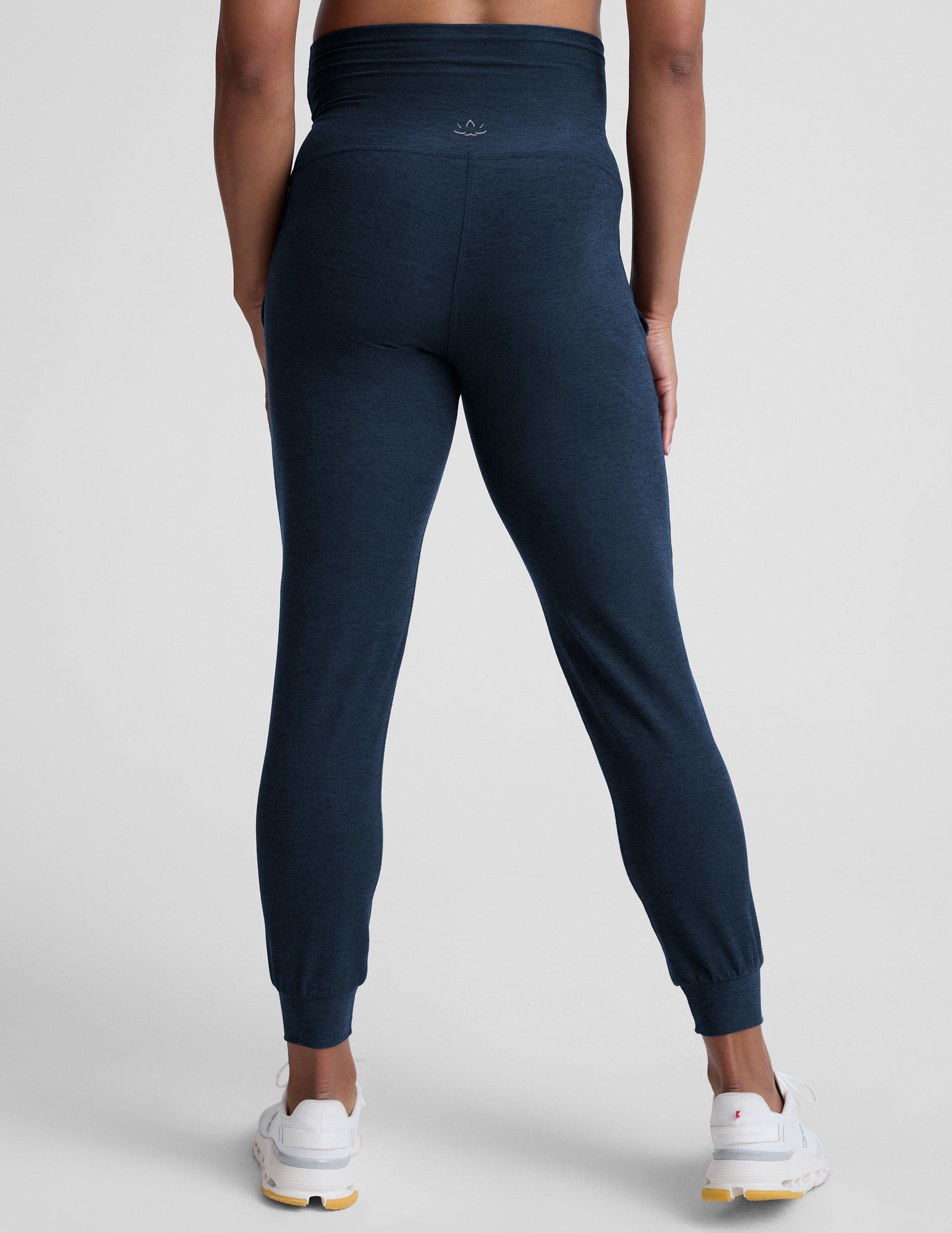 pregnant woman wearing navy blue maternity joggers with pockets on a plain background.