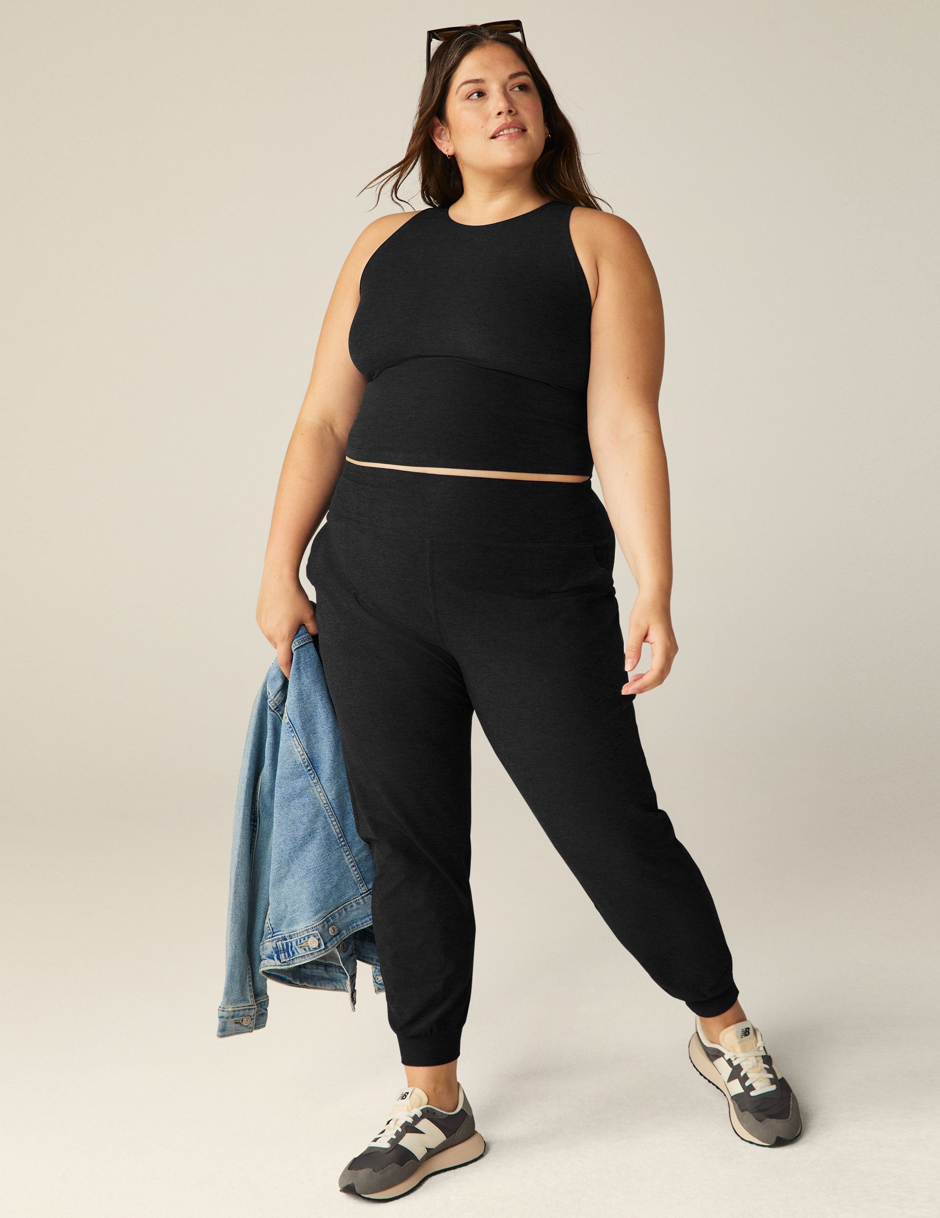 Woman wearing black Spacedye Midi Joggers with a wide waistband and tapered, banded cuffs, holding a denim jacket.