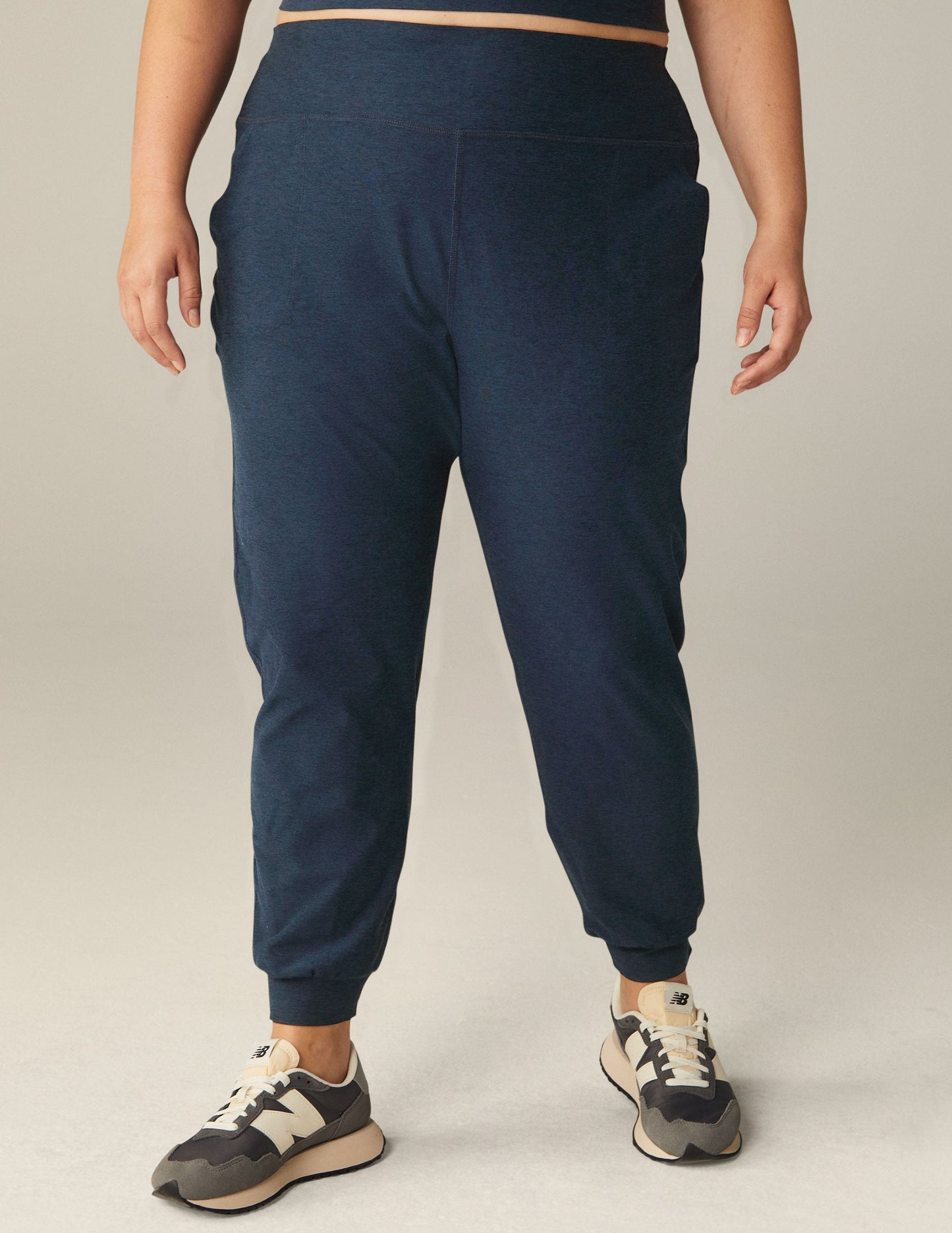 A person wears Nocturnal Navy Spacedye Midi Jogger pants with a wide waistband, tapered legs, and banded cuffs.