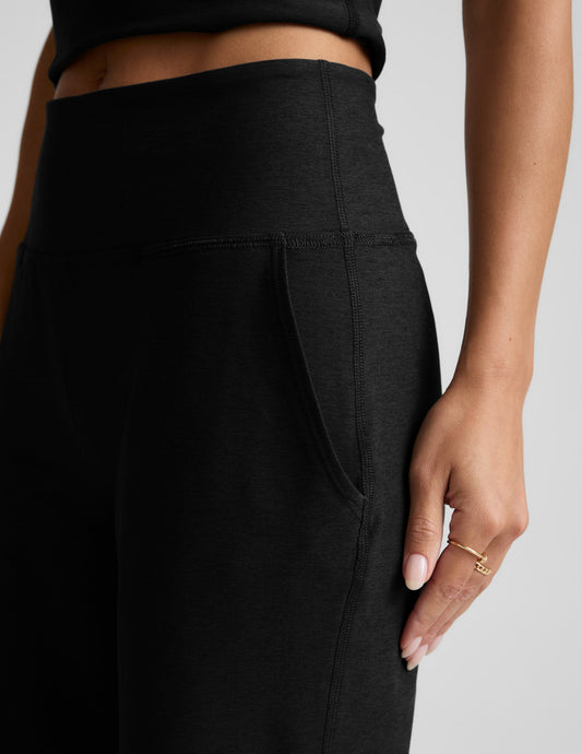 Person wearing black pants with a plain background.