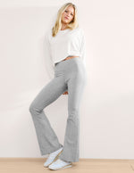 Woman wearing a white top and gray pants against a plain background.