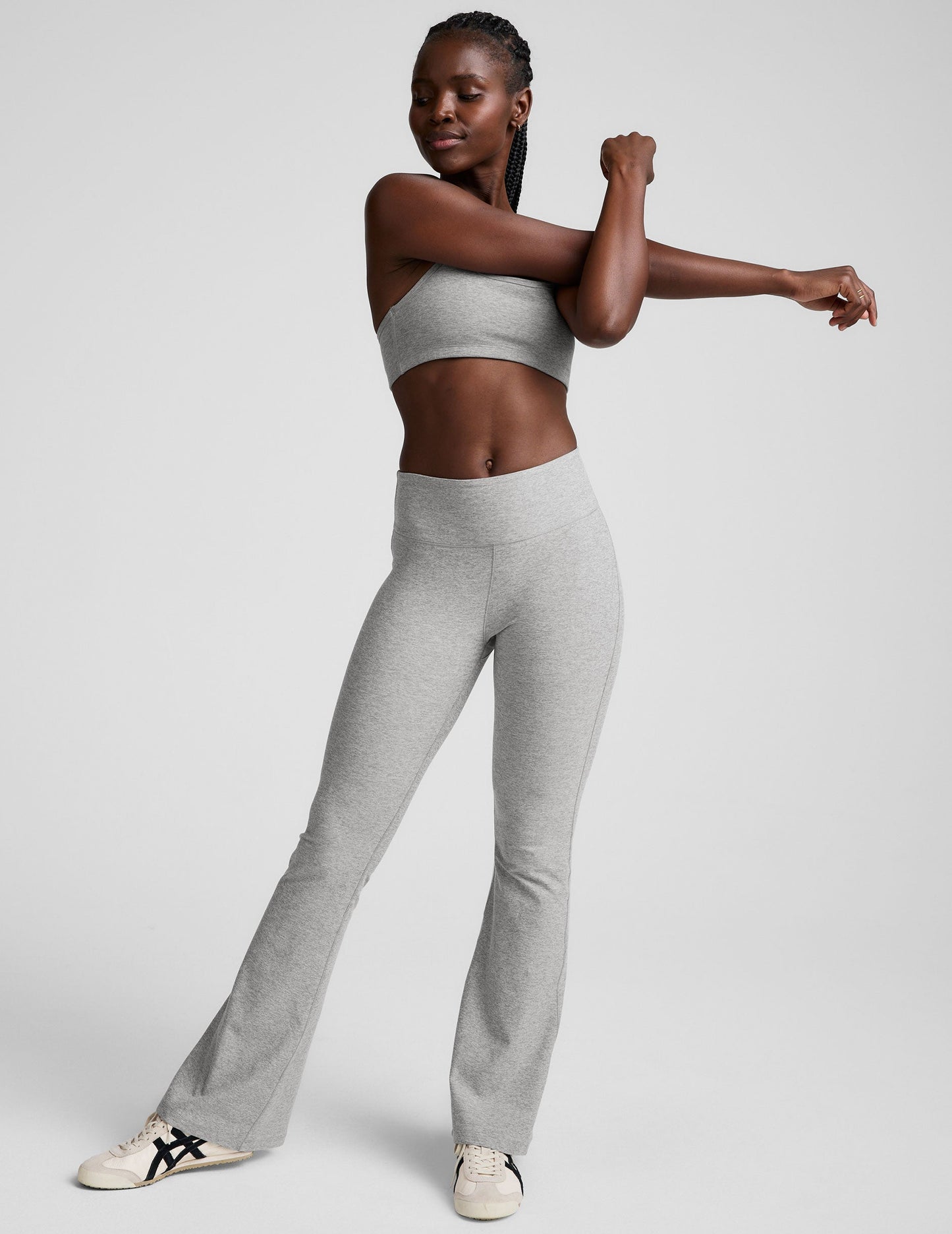 Woman stretching in gray Spacedye Mid-Rise Bootcut Pant. Snug marled fabric with a wide waistband and flared legs.
