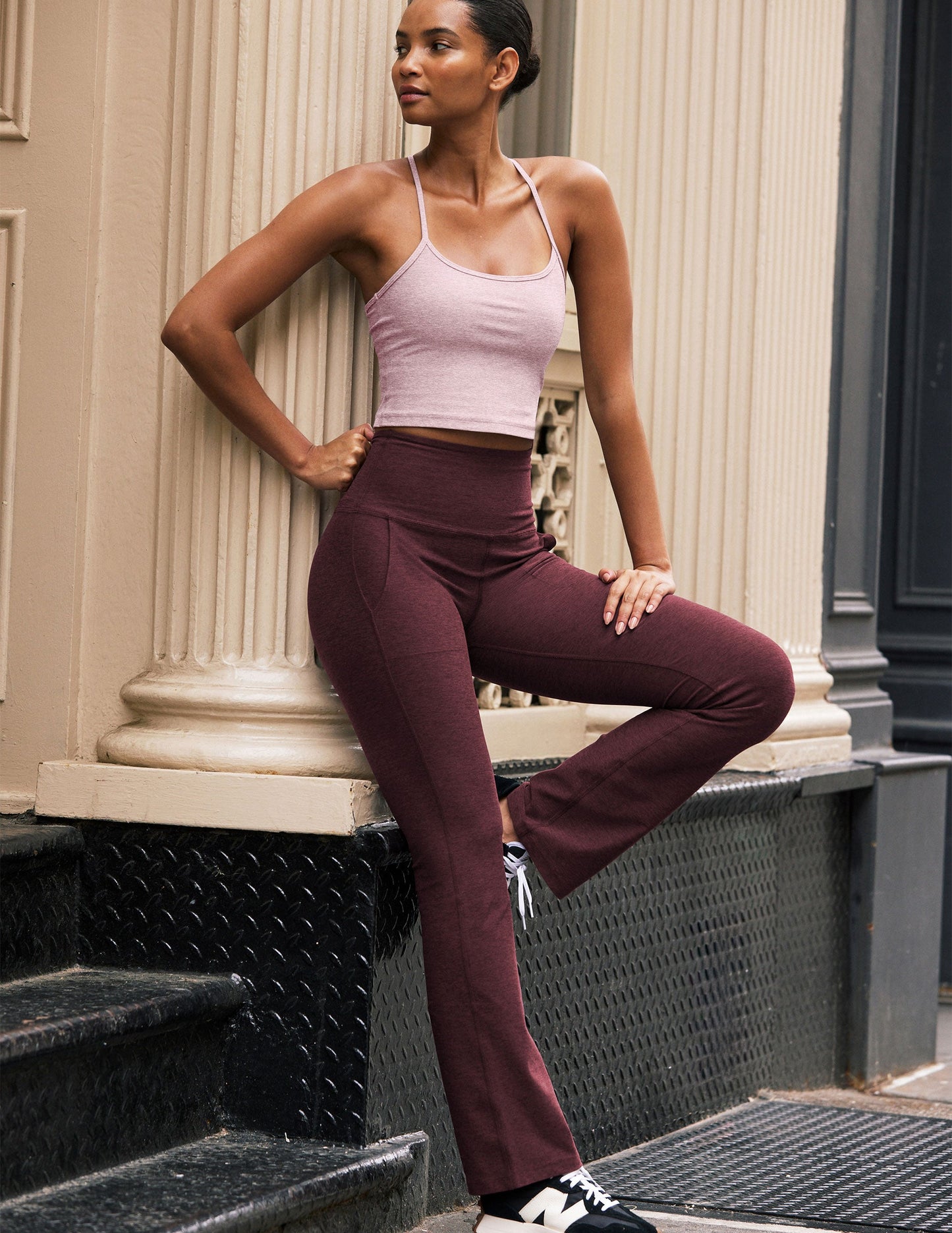 Woman wearing Maroon/Burgundy Spacedye™ High Waisted Practice Pocket Bootcut Pant paired with a pink tank top and sneakers.