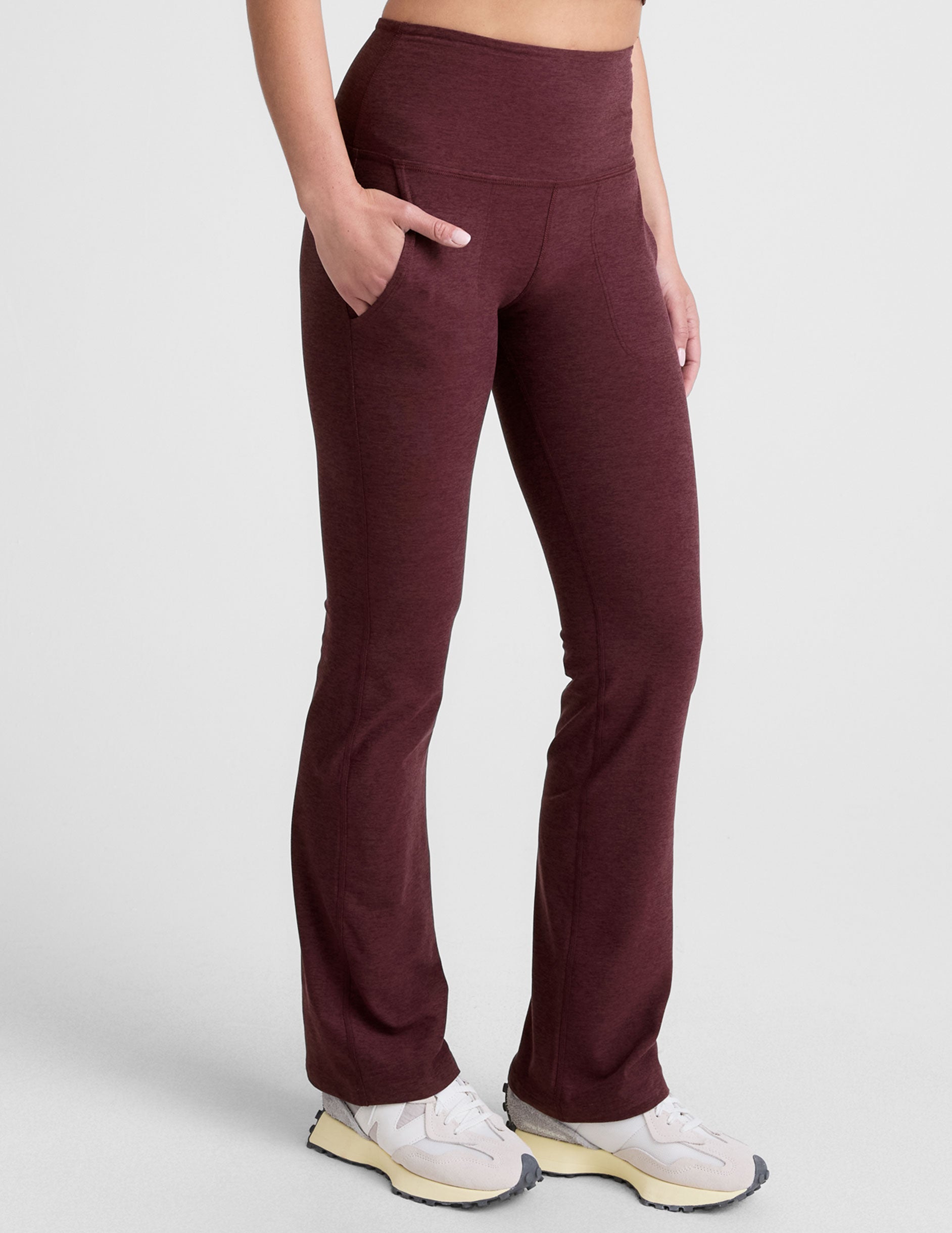 Woman wearing Maroon Spacedye™ High Waisted Practice Pocket Bootcut Pant with hands in pockets and cream sneakers.