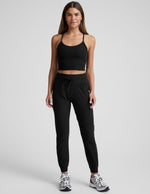 Woman wearing black Spacedye Go Pocket Jogger with high drawstring waist and cuffed ankles, standing against grey background.
