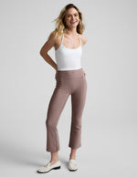 Smiling woman wears brown Spacedye Pintuck Kick Flare High Waisted Pant with front seams and a wide waistband in a studio.