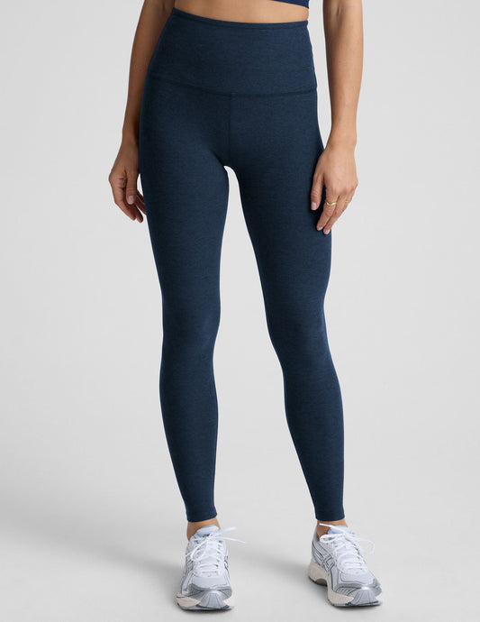 woman is wearing blue high-waisted midi length leggings against a plain background.