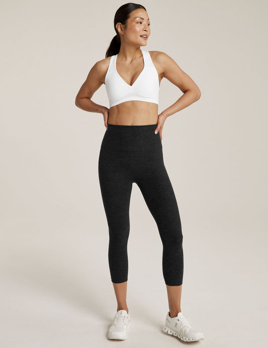 Model wears Spacedye Walk And Talk High Waisted Capri Legging in dark marled grey with white sports bra and sneakers.