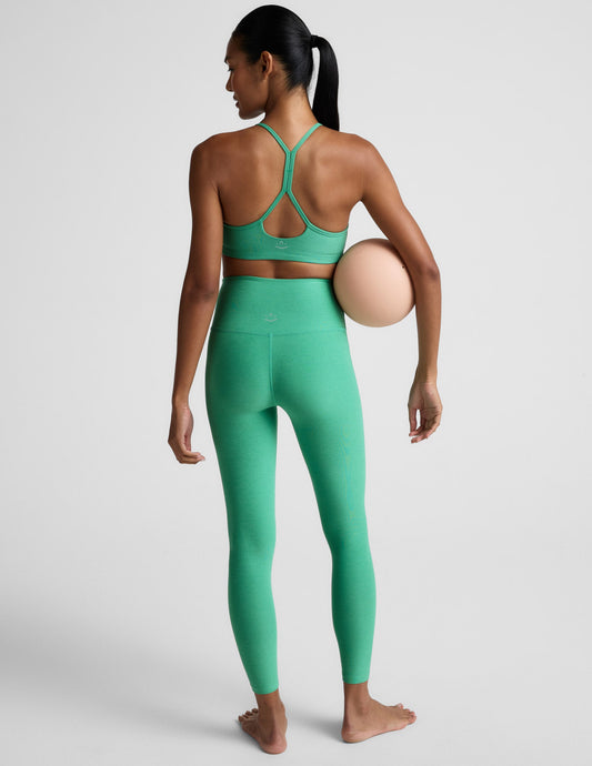 Woman wearing a green bra and green high-waisted midi leggings against a plain background.