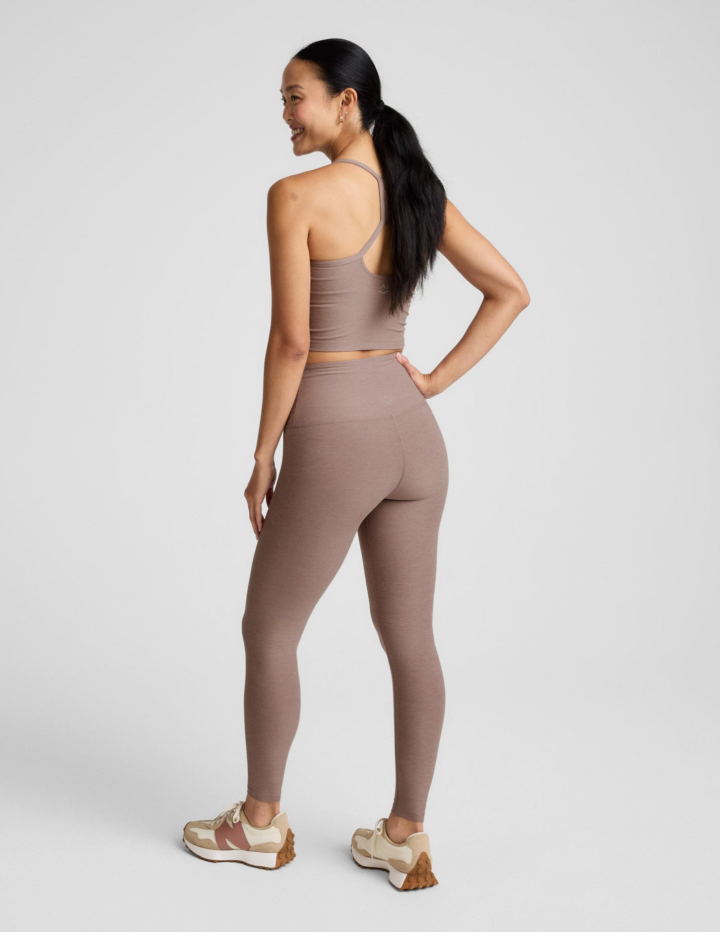 Woman wearing a brown cropped tank and leggings against a plain background.