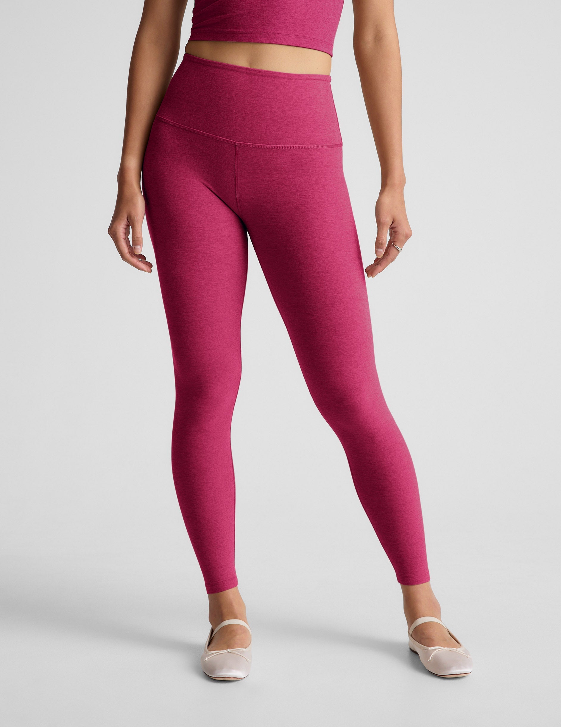 Woman wearing a red cropped tank and leggings against a plain background.