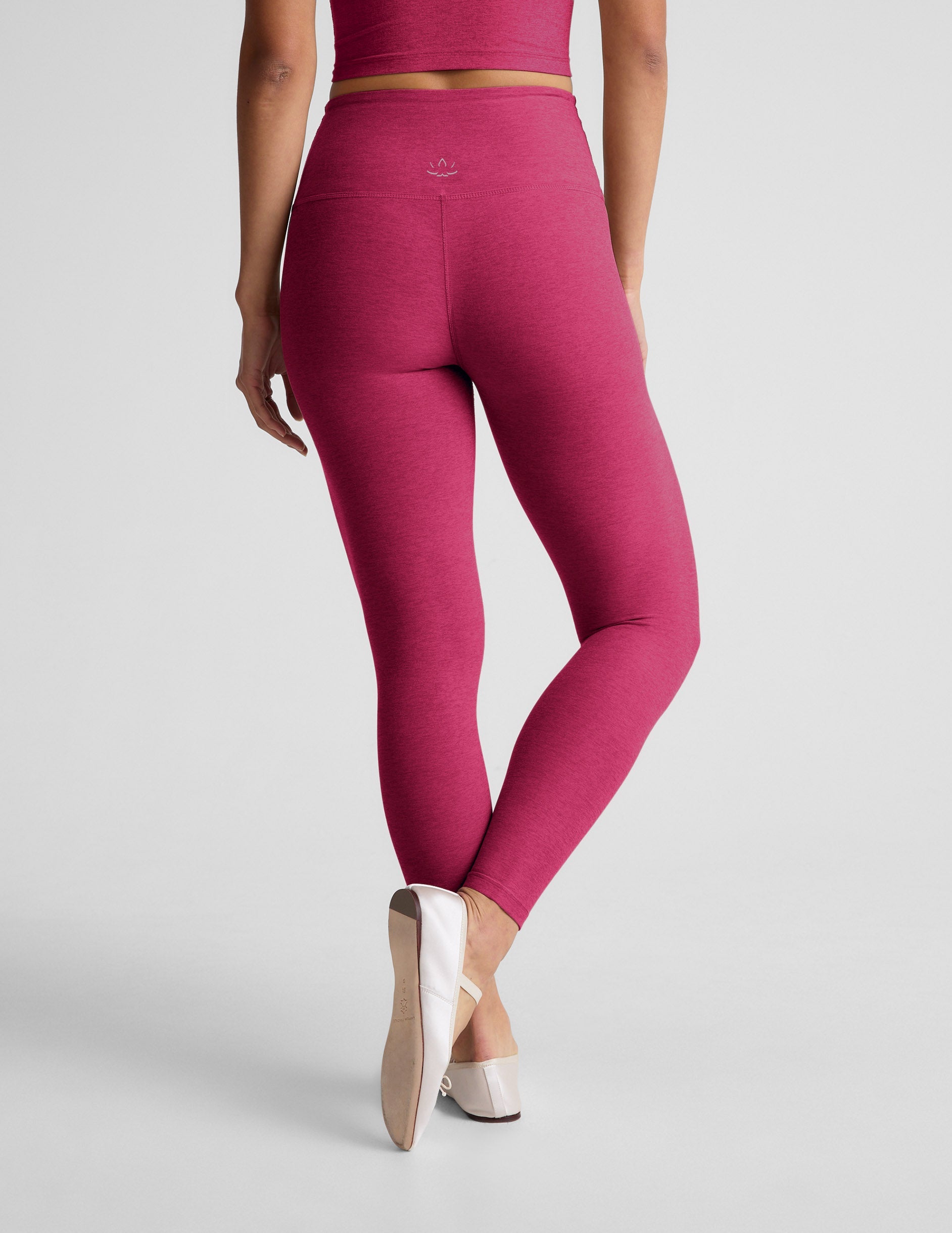 Woman wearing a red cropped tank and leggings against a plain background.