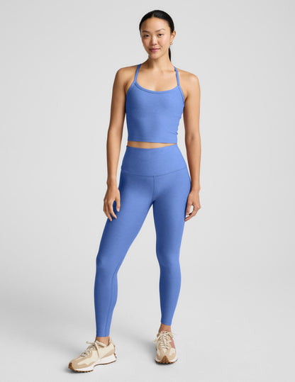 Woman wearing a blue cropped tank and leggings against a plain background.