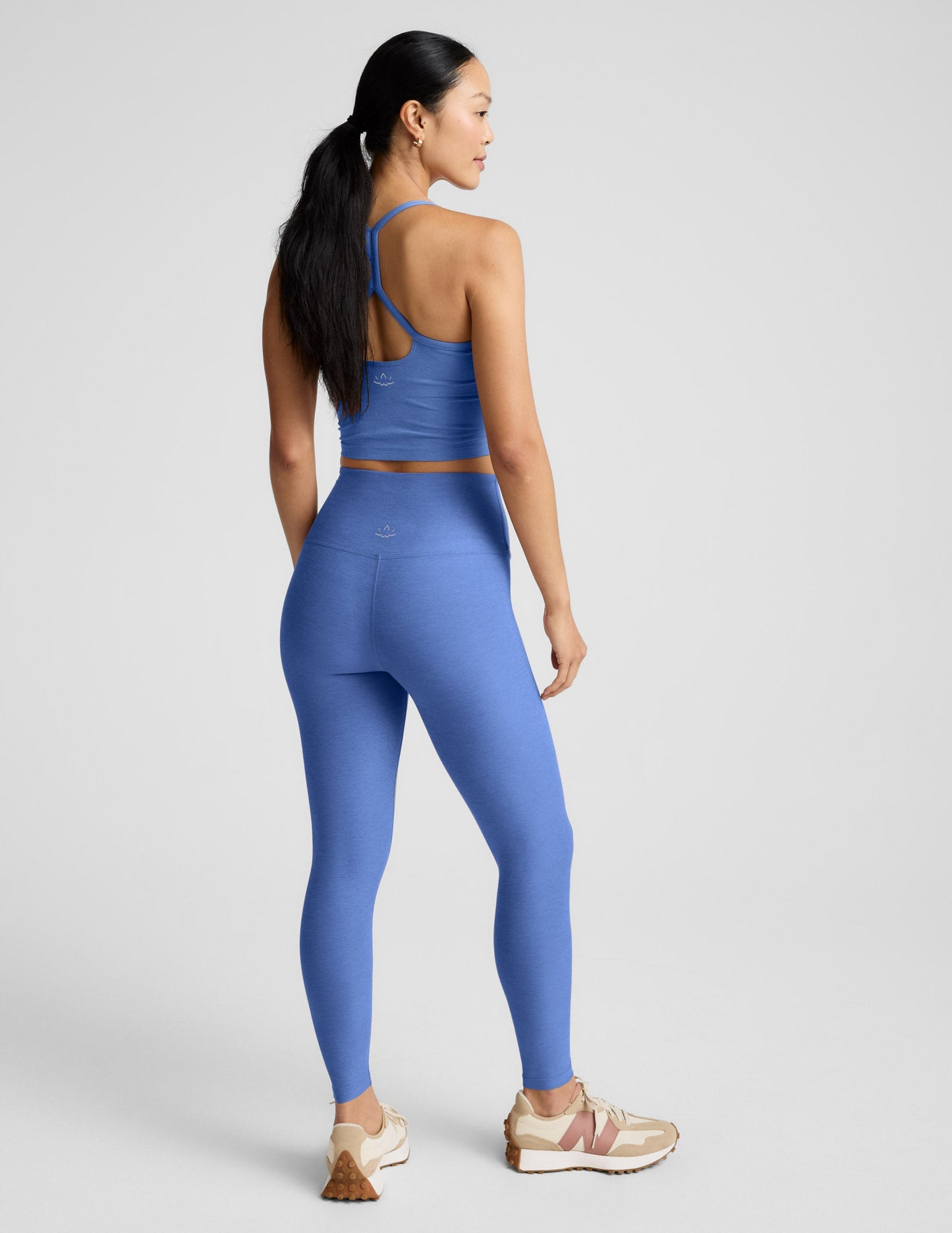 Woman wearing a blue cropped tank and leggings against a plain background.