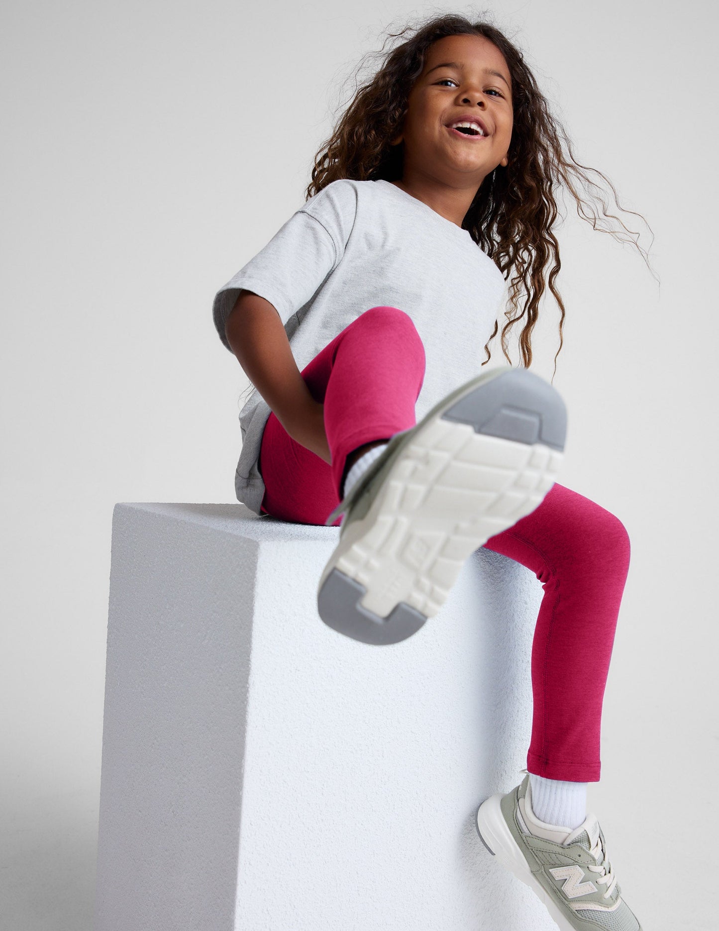 Young girl wearing a white t-shirt and red leggings on a light gray background.