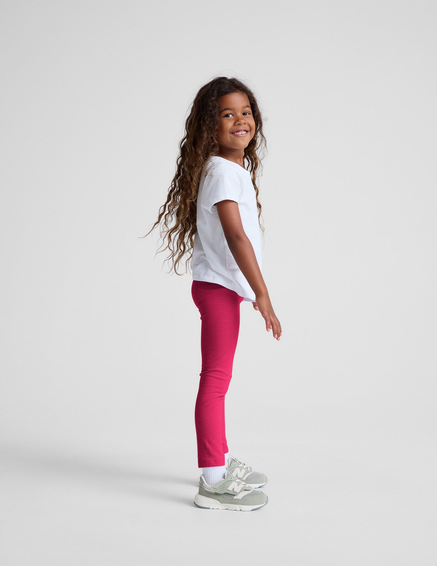 Young girl wearing a white t-shirt and red leggings on a light gray background.