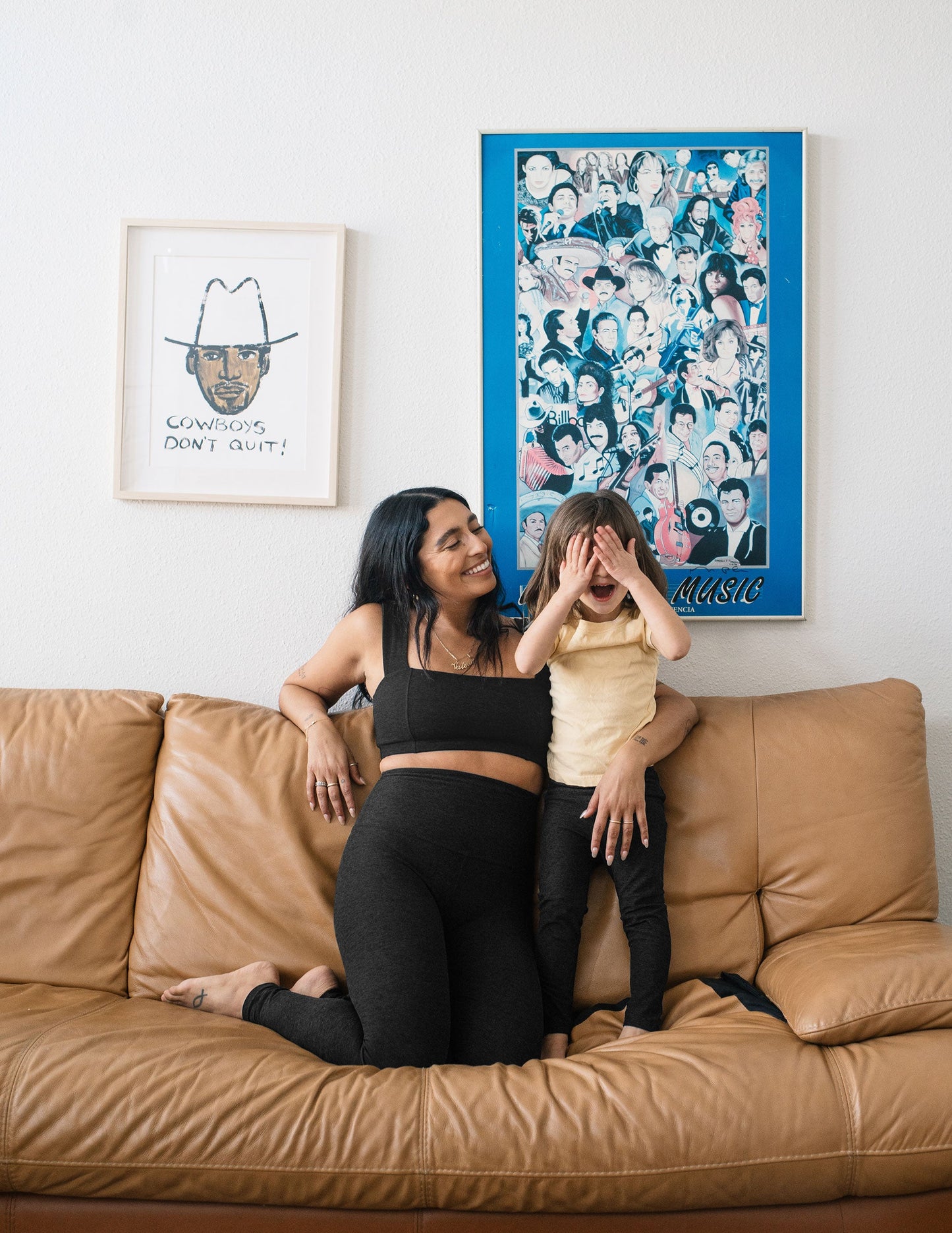 A toddler in black Spacedye Toddler Legging plays on a tan couch with a woman in matching Darkest Night marled activewear.