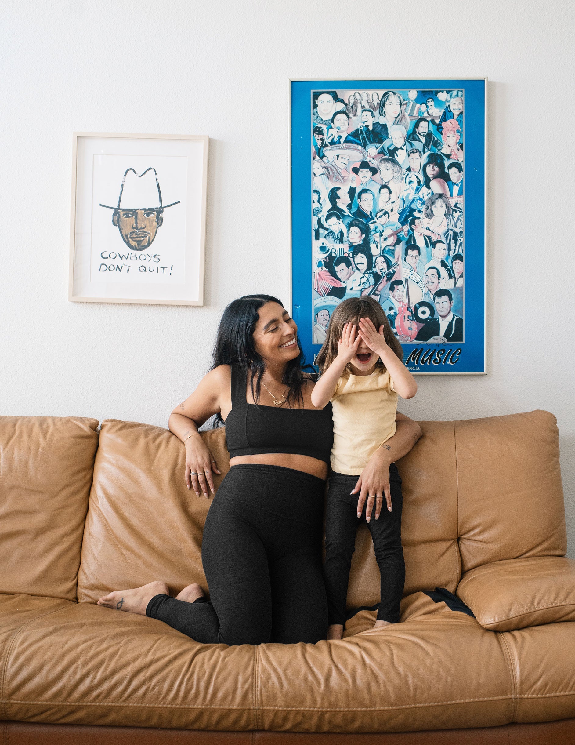 A toddler in black Spacedye Toddler Legging plays on a tan couch with a woman in matching Darkest Night marled activewear.