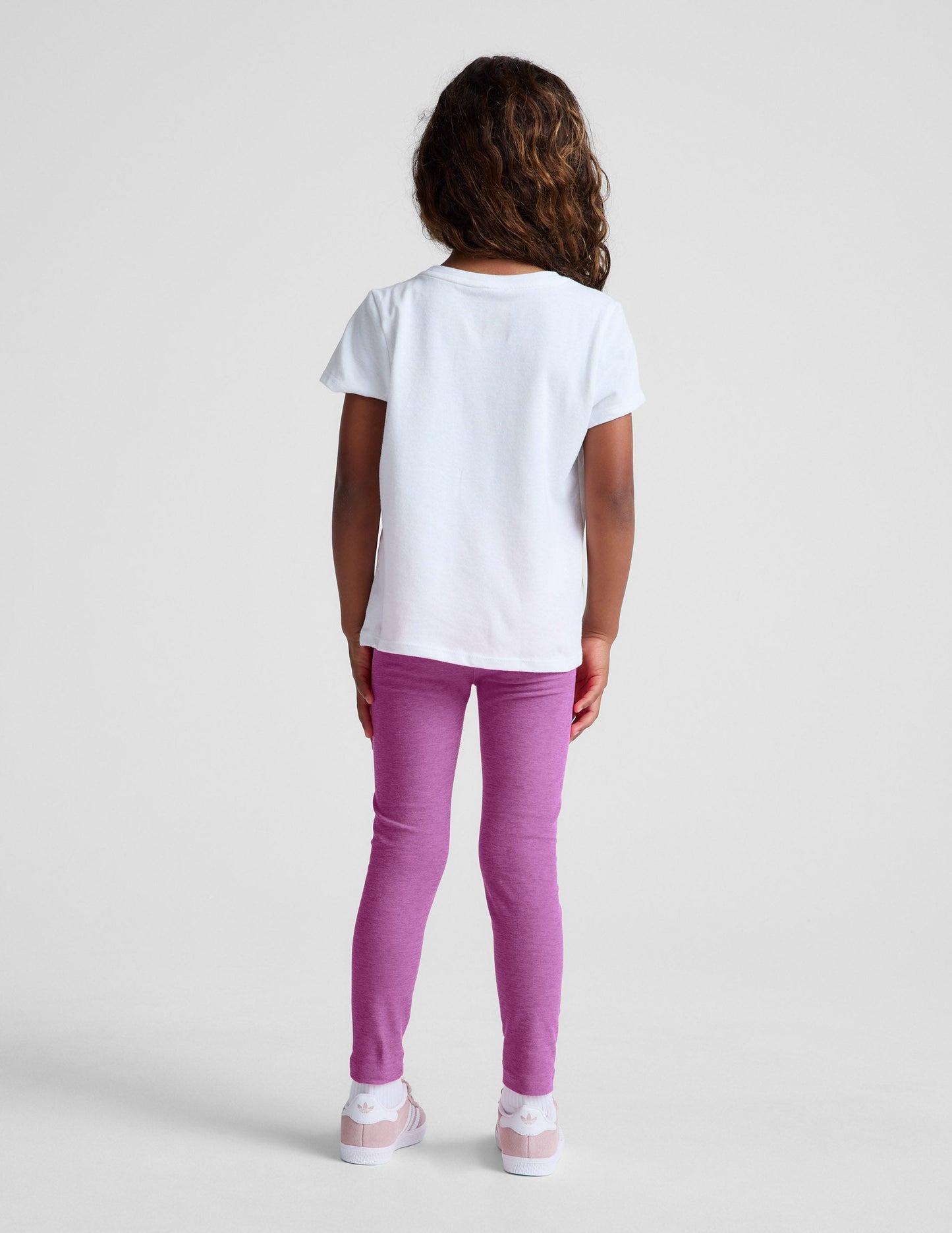 Rear view of girl wearing purple Spacedye Toddler Legging™ paired with a white t-shirt and pink sneakers.