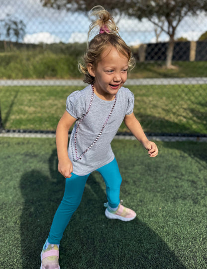 Girl wearing Blue Spacedye Toddler Legging™ paired with a grey puff-sleeve shirt and sneakers while playing.
