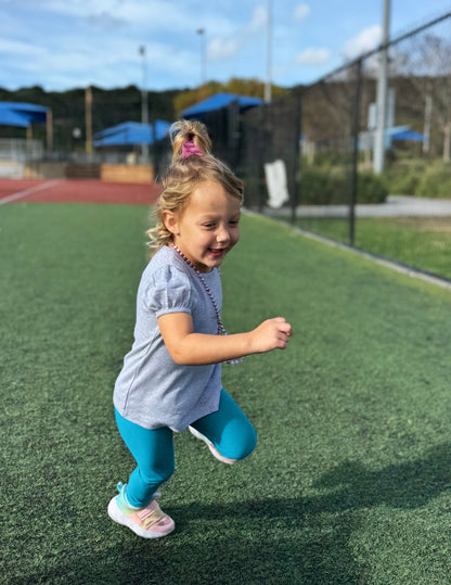 Toddler girl running in Blue Spacedye Toddler Legging™ paired with a grey puff-sleeve shirt and colorful sneakers.