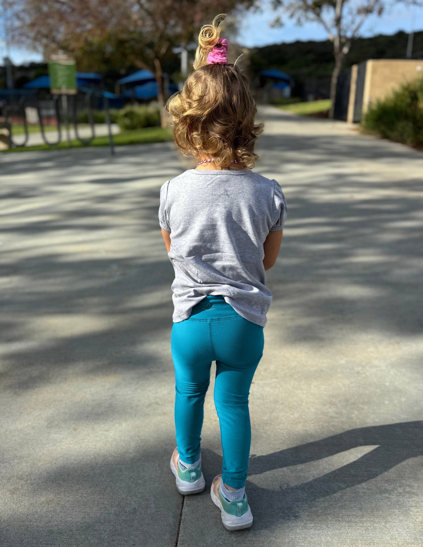 Rear view of girl wearing Blue Spacedye™ Toddler Legging with a grey short-sleeve t-shirt and sneakers.