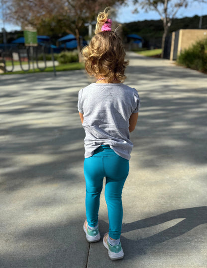 Rear view of girl wearing Blue Spacedye™ Toddler Legging with a grey short-sleeve t-shirt and sneakers.