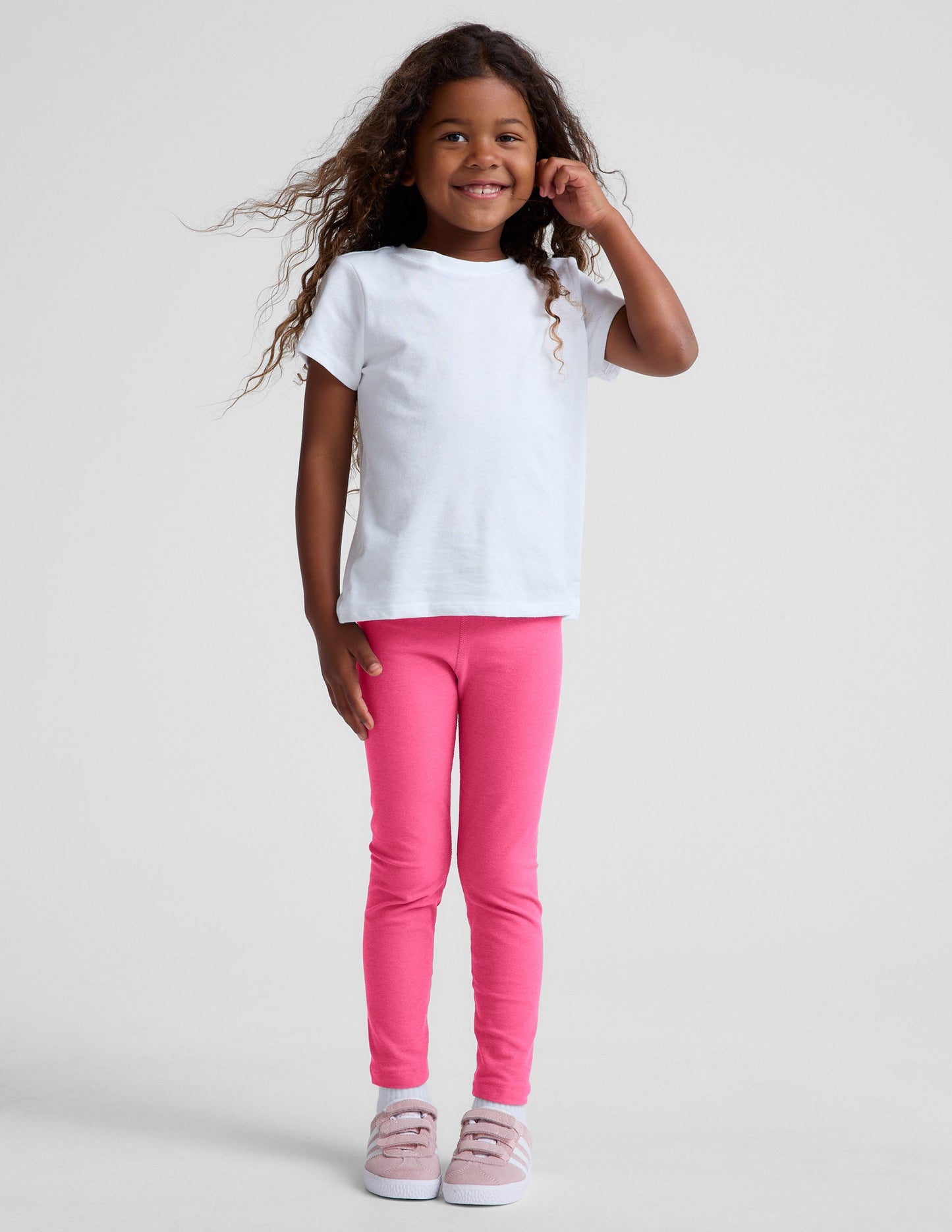 Girl wearing Pink Spacedye™ Toddler Legging paired with a white t-shirt and pink sneakers.
