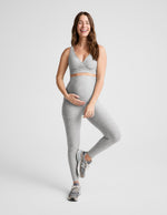 Pregnant woman wearing a gray bra and leggings on a plain background.